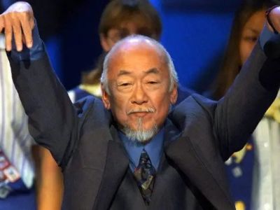 Pat Morita is doing the iconic crane kick pose.